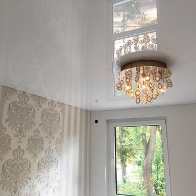 Spanndecke mit glänzender Oberfläche und einer eleganten Deckenlampe.